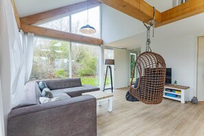 A modern living room with a sofa, a hanging chair, and a TV stand. - Coastal Family Escape with Enclosed Garden (Renesse)