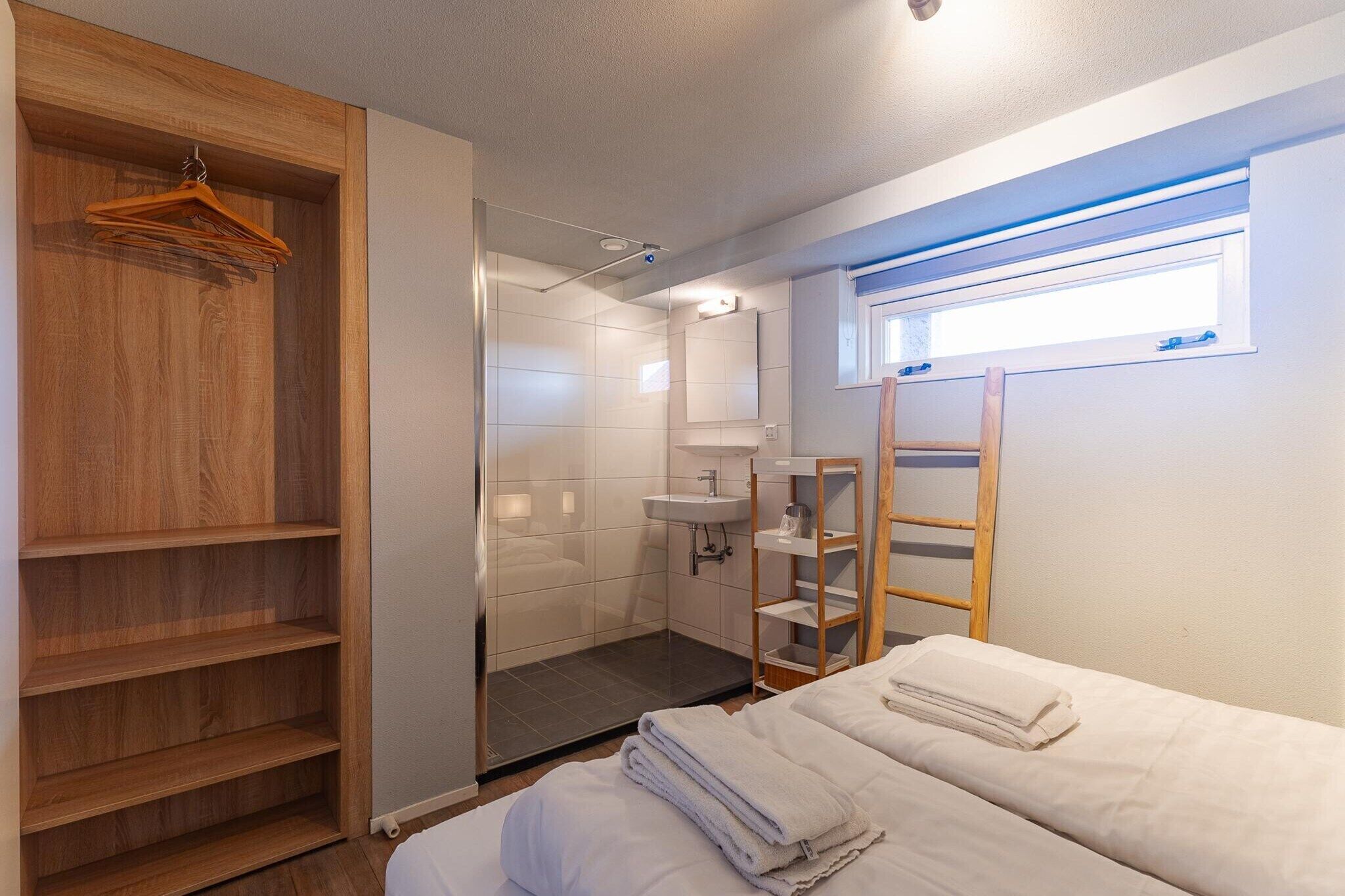 A hotel room with a wooden wardrobe, a shower area, a bed with towels, and a window with blinds.