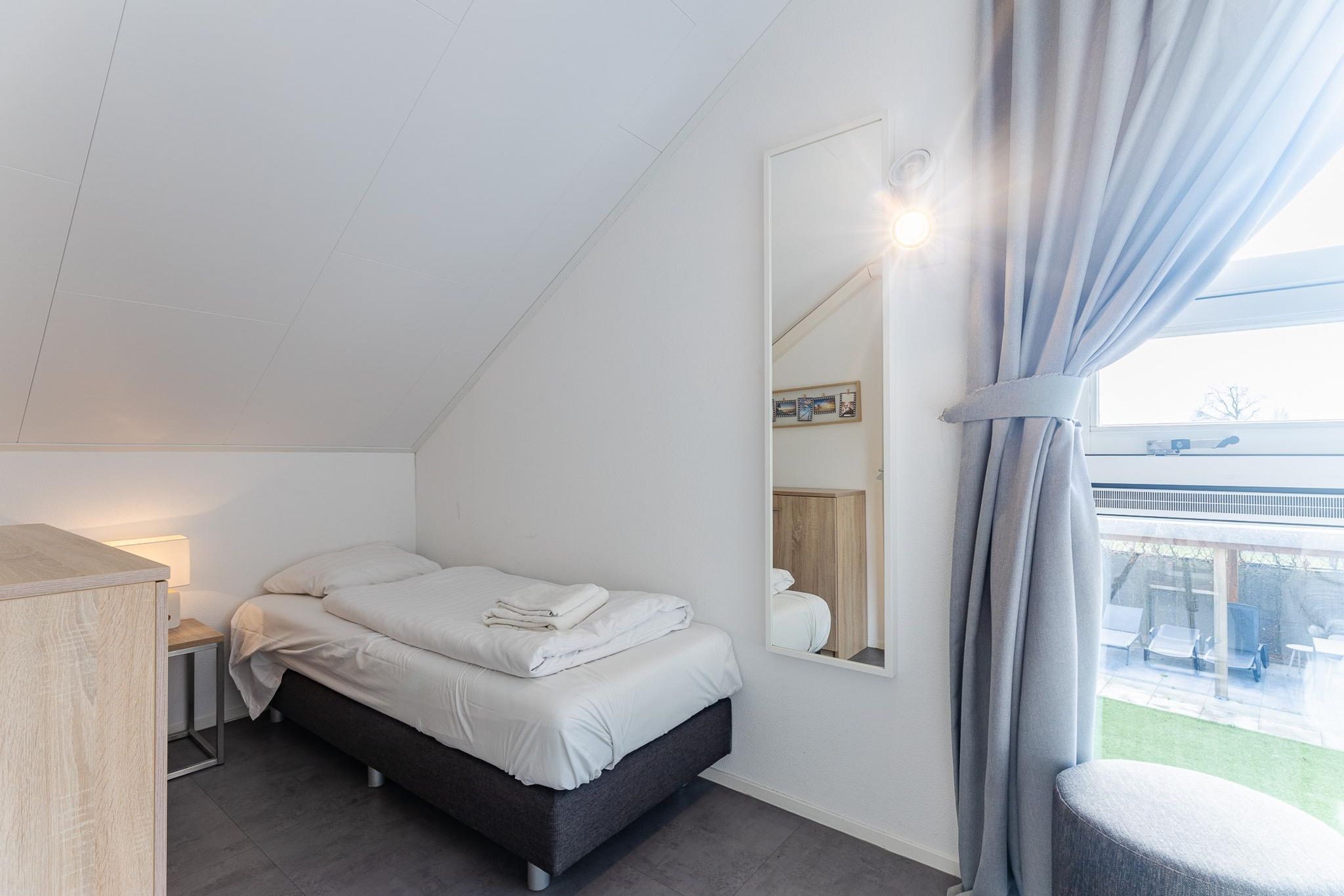 Un dormitorio con cama, mesita de noche, lámpara y vistas al exterior.
