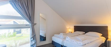 Un dormitorio con cama, lámpara de noche, ventana con cortinas y vistas al exterior.