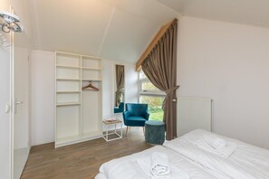 Ein Schlafzimmer mit einem Bett, einem Sessel, einem Kleiderschrank und einem Fenster mit Vorhängen.