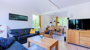 Uma sala de estar moderna com um sofá de couro preto, mesa de centro de madeira e uma TV sobre um armário de madeira.