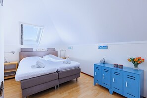 Ein Schlafzimmer mit einem Bett, einem Fenster, einem Nachttisch, einer Kommode und einer Wanduhr.