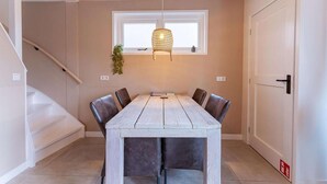 Zona pranzo con tavolo in legno, sei sedie, lampadario, finestra e porta.