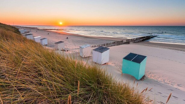 Una spiaggia con file di strutture bianche, un molo di legno e un tramonto.