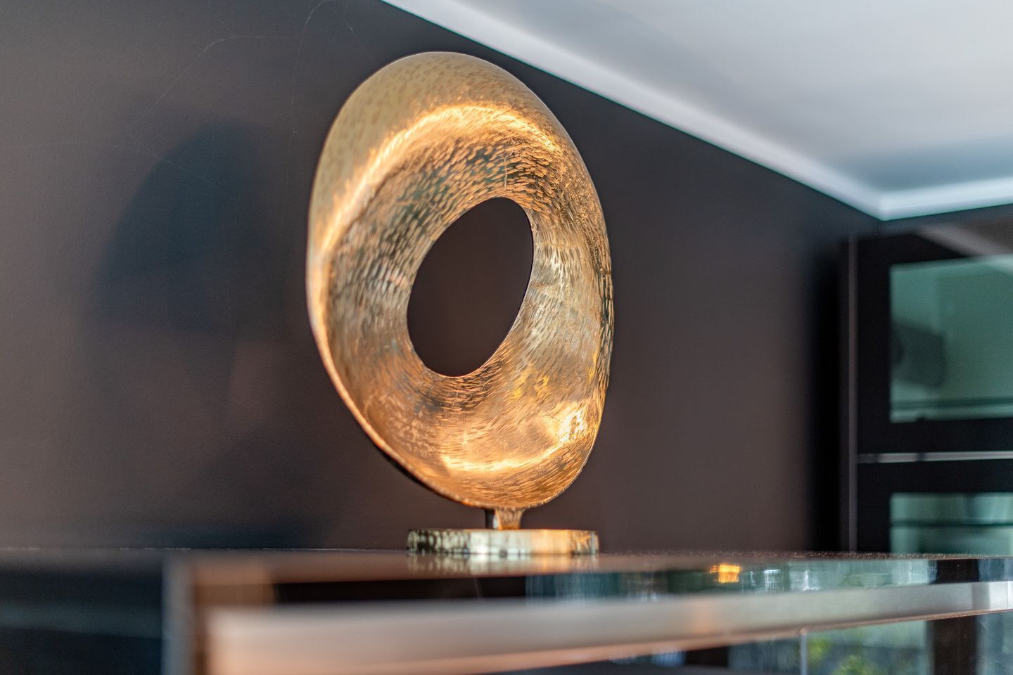 Een metalen, ronde sculptuur met een reflecterend oppervlak, gemonteerd op een voet.