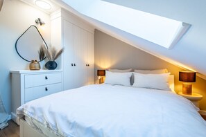 A bedroom with a skylight, a bed with white bedding, two bedside tables with lamps, a white wardrobe, and decorative items on the dresser. - Fanderhüs - Fanderhüs in Westerland (Sylt)