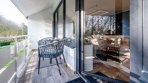 En modern balkong med en glasdörr som leder ut till en utomhusplats med sittmöbler, och som har en stenmur och ett trägolv.