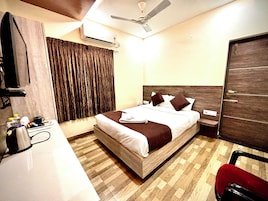 Una habitación de hotel con cama, un escritorio y silla, aire acondicionado, ventilador de techo y una puerta.