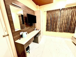 Un baño moderno con un espejo grande, un televisor de pantalla plana, un tocador con lavabo y una zona de ducha.