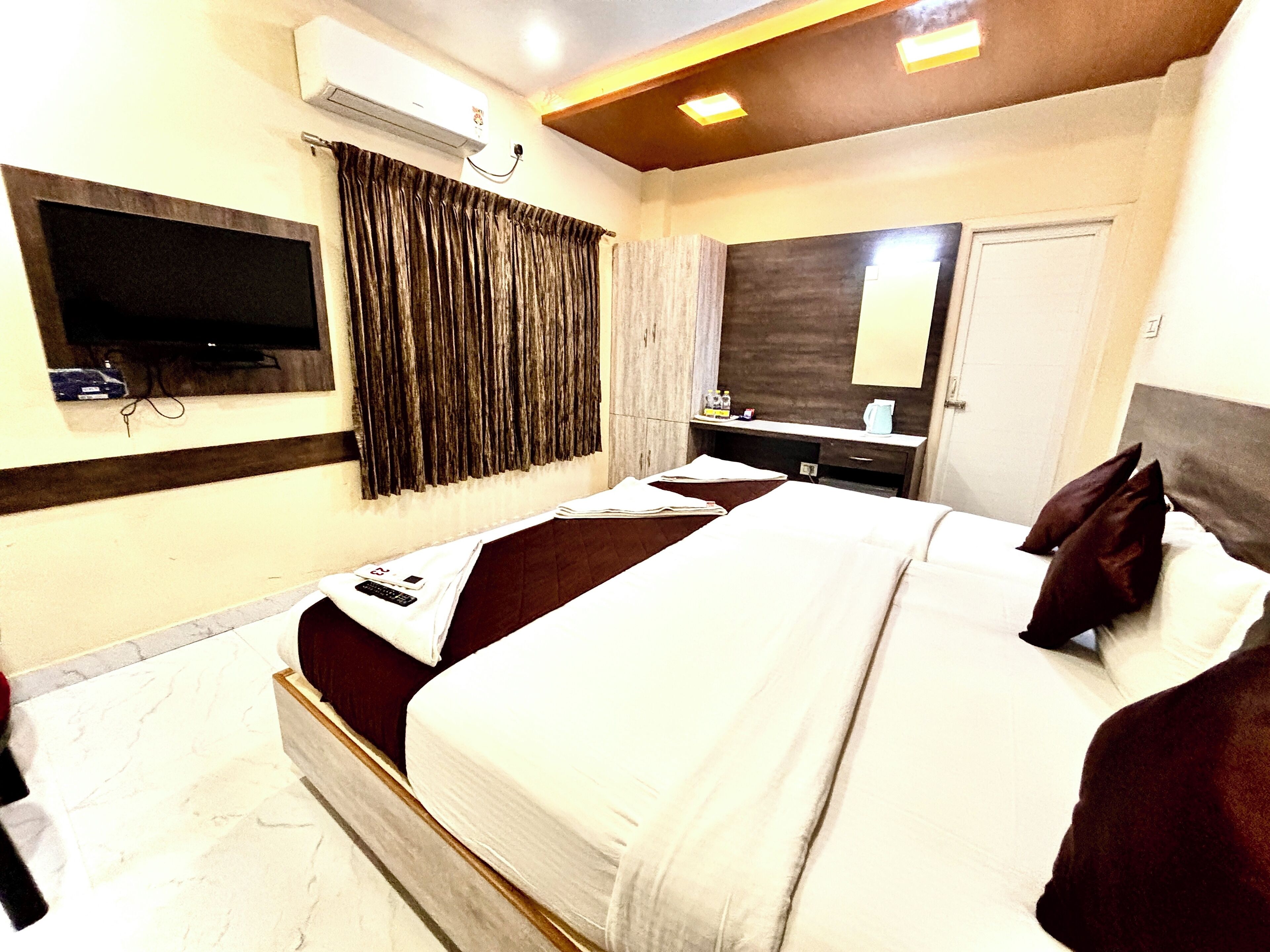 A hotel room with a large bed, a TV mounted on the wall, a mirror, and a window with curtains.