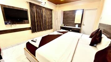 Habitación de hotel con una cama grande, un televisor montado en la pared, un espejo y una ventana con cortinas.