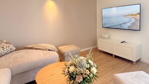 Un salon avec un canapé, une table basse ornée de fleurs, un téléviseur fixé au mur et un petit meuble.