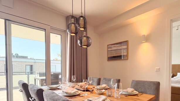 Un coin repas avec une table en bois, des chaises à revêtement gris et une vue à travers une porte vitrée.