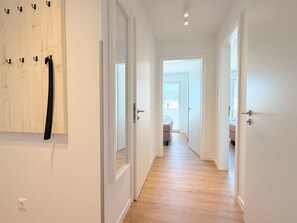 A hallway with wooden flooring, white walls, and a door leading to a room with a bed and a window. - 2170 - Gode Ström quarters "Söven" - Penthouse Strandwiese - 2170 - Gode Ström (Dahme)