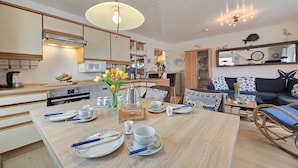 A modern kitchen with a dining area, wooden furniture, and a ceiling fan. - Vacation apartment Lüttje Mööv Norddeich - Comfortable vacation apartment Lüttje Mööv (Norden)