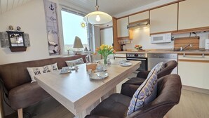A modern kitchen with a central island, wooden cabinets, and a dining area with a bench and chairs. - Vacation apartment Lüttje Mööv Norddeich - Comfortable vacation apartment Lüttje Mööv (Norden)