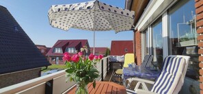 A balcony with a table, chairs, a polka-dotted umbrella, and a vase of flowers. - Vacation apartment Lüttje Mööv Norddeich - Comfortable vacation apartment Lüttje Mööv (Norden)