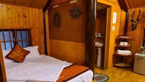 A wooden cabin-style room with a bed, a wooden wall with a decorative plate, a mounted deer head, and a small refrigerator. - Cat Ba Mountain View Homestay (Hai Phong)