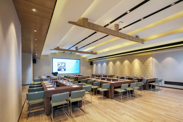 A conference room with multiple tables and chairs, a large screen for presentations, and a wooden ceiling design. - Echarm Hotel (Chengdu)