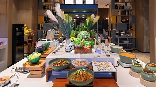 Un'impostazione buffet con diversi piatti, un'elegante composizione floreale al centro e una moderna area cucina sullo sfondo.