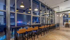 Zona bar moderna con diverse opzioni di seduta e ampie finestre che offrono vista sulla città.