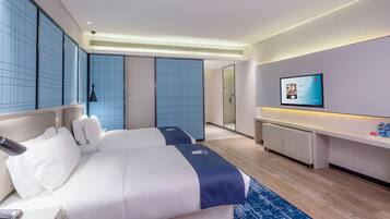 A modern hotel room with two beds, a TV, a desk, and a bathroom visible through a sliding door.