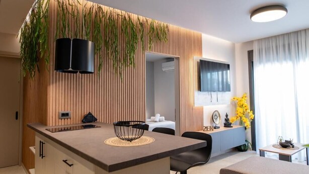 Et moderne køkken med en central ø, træpaneler, hængende planter og et spiseområde med et bord og stole.