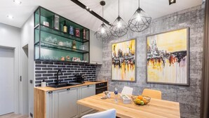 A modern kitchen with a brick backsplash, wooden countertop, and a dining area with a table and chairs. There are two large abstract paintings on the wall. - Boutique Hotel Casa Verdi (Veliko Tarnovo)