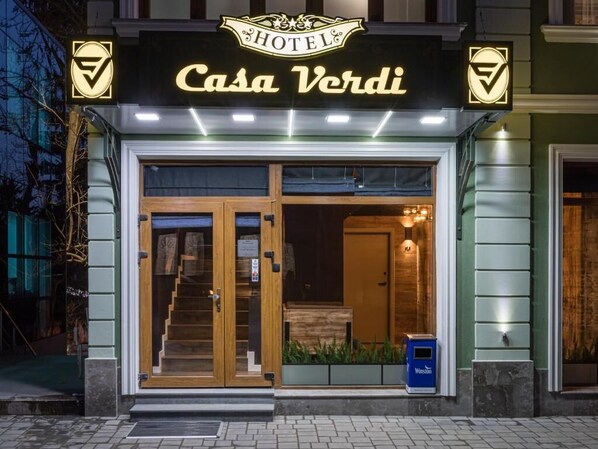 A hotel entrance with a sign reading "Casa Verdi" and a logo on the sides.