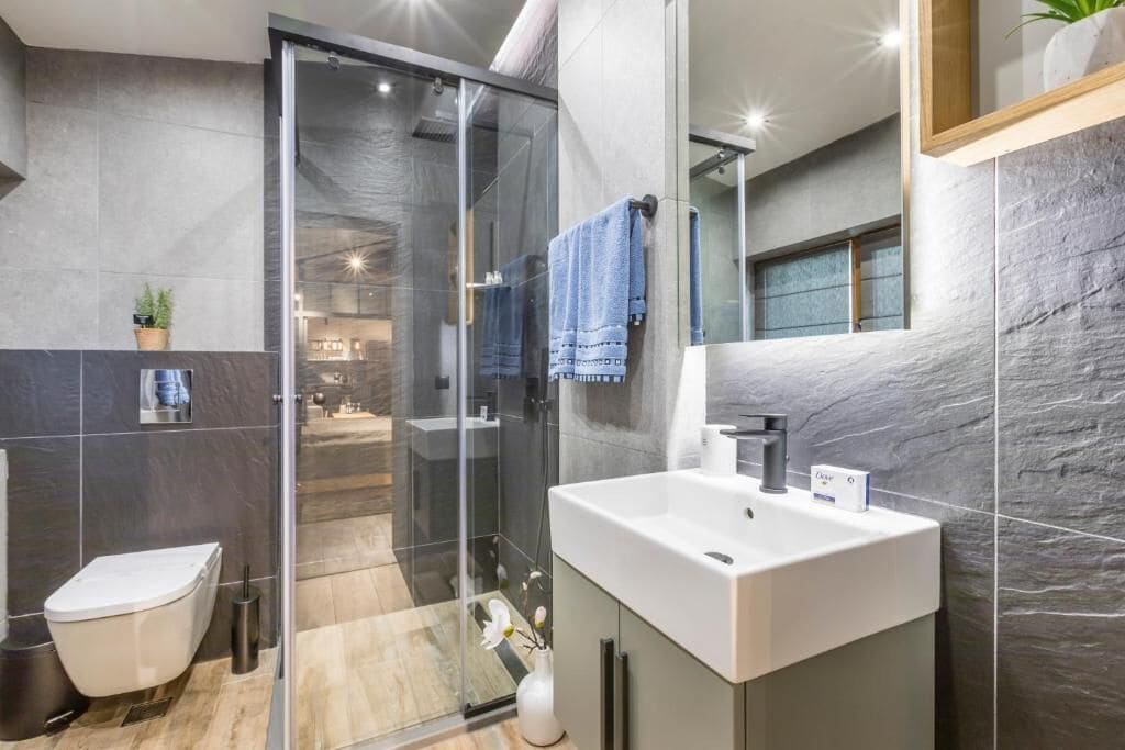A modern bathroom with a glass shower enclosure, a white sink, and a large mirror.