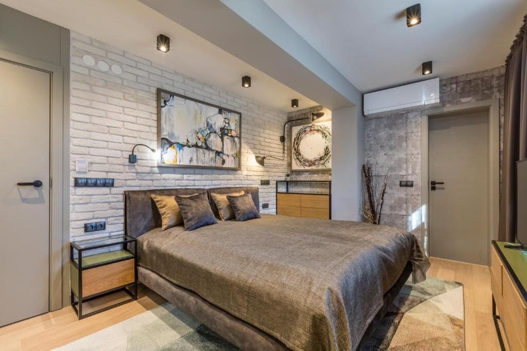 A modern bedroom with a large bed, a brick wall, and artwork.