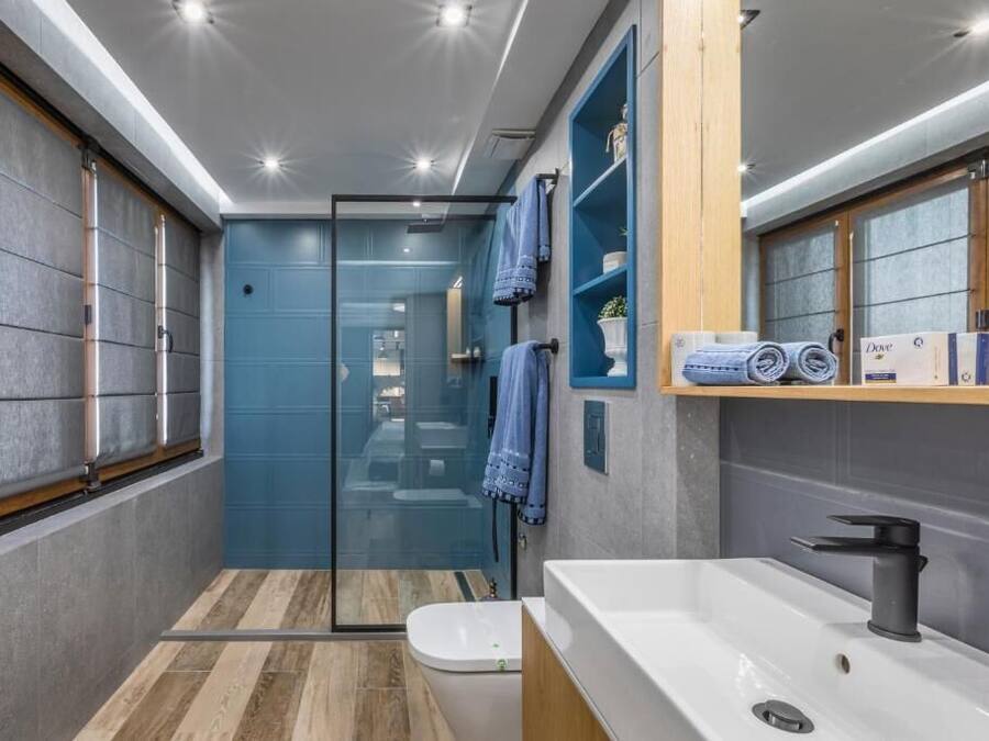 A modern bathroom with a glass shower enclosure, a white sink, and wooden shelves with towels.