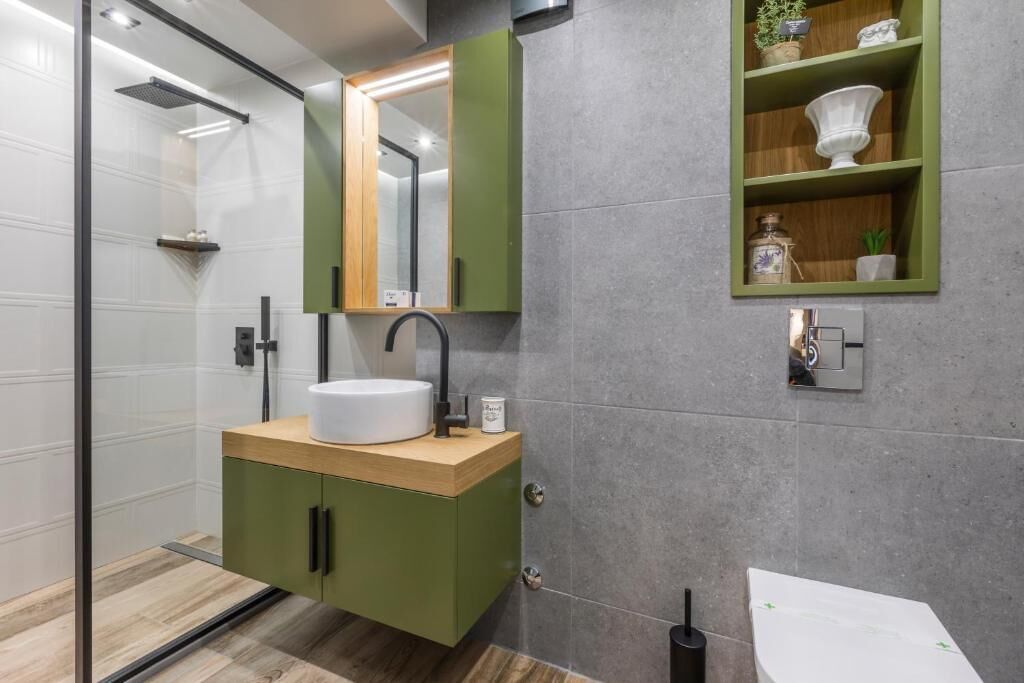A modern bathroom with a glass shower enclosure, a wooden vanity with a white sink, and a green cabinet.