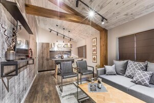 Una sala de estar moderna con un sofá, sillas, una mesa de centro y una cocina al fondo.