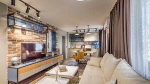 A modern living room with a brick wall, a flat-screen TV, a sofa, a coffee table, and a dining area with a yellow chair. - Boutique Hotel Casa Verdi (Veliko Tarnovo)