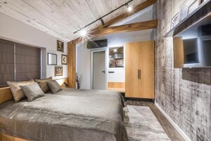 Un dormitorio moderno con una cama grande, vigas de madera y una pared de concreto decorativa.