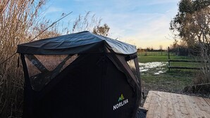 A black tent with the brand 'NORLIVA' on the side, set on a wooden deck with a grassy field and trees in the background. - Nordic Experience: Sauna & Cold Bath in the Camargue (Arles)
