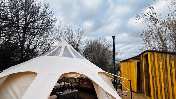 A tent with a dining area inside, a wooden deck, and a small wooden structure in the background.