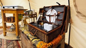 A tent interior with a wicker basket containing a plate, cups, and a bottle.