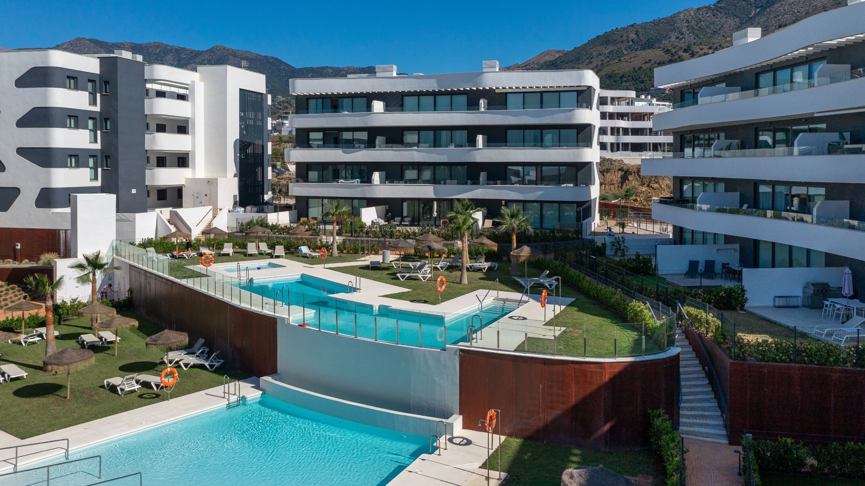 Ett modernt hotell med flera balkonger, ett poolområde och utsikt över bergen.