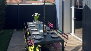 Eine Terrasse mit Esstisch, Gartenstühlen, einem großen Sonnenschirm und einer Weinflasche.