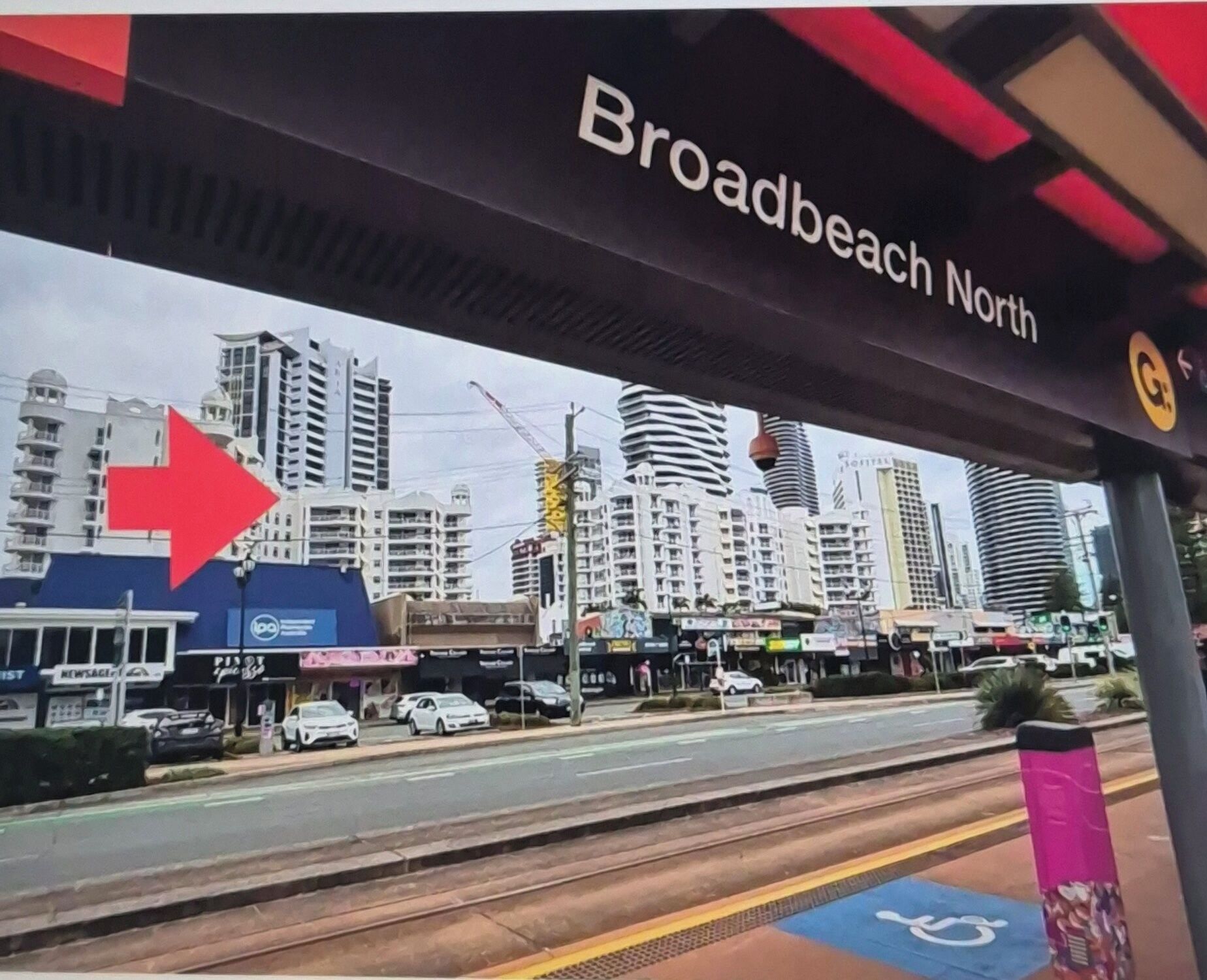 A bus stop with a sign reading "Broadbeach North" and a red arrow pointing left.