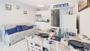 A compact living space with a kitchenette, a dining area, and a sofa with striped cushions. - Apartment with sea view, 2 adults and 2 children (Saint-Gilles-Croix-de-Vie)