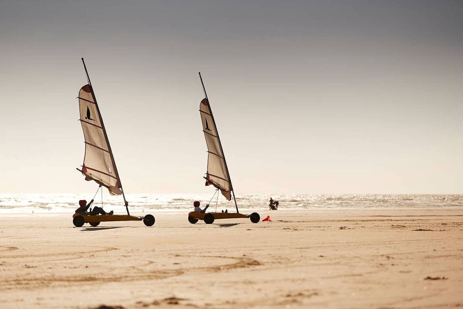 Two sailboats on a sandy beach with the ocean in the background.