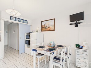 Ein Essbereich mit einem Tisch für vier Personen, weißen Stühlen, einem weißen Schrank mit Schubladen, einem flachbildfernseher an der Wand und einem gerahmten Gemälde über dem Tisch.