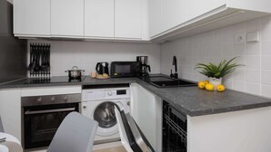 Eine kleine Küche mit weißen Schränken, einem Backofen, einer Waschmaschine und einem Spülbecken.