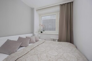 Un dormitorio con una cama grande, una ventana con persianas, un radiador y una planta en maceta en el alféizar.
