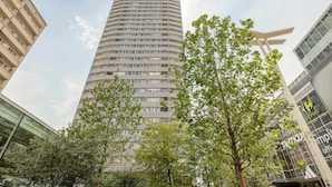 Ein hohes, modernes Gebäude mit einer gewölbten Fassade, umgeben von Bäumen und weiteren Gebäuden.