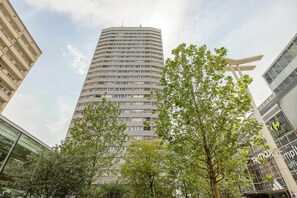 Un edificio alto y moderno con fachada curva, rodeado de árboles y otros edificios.